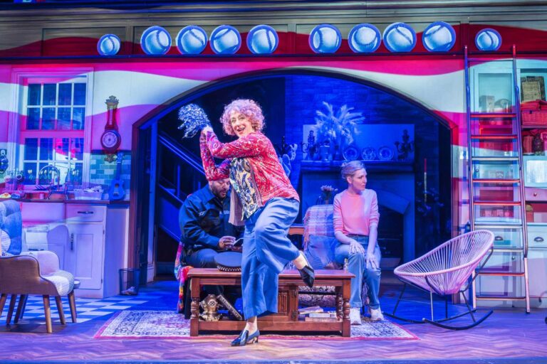 Dame Maureen Lipman as Allegra dancing while Bailey Patrick as Officer Rogers and Elizabeth Bower as Anna watch from the cottage sitting room.