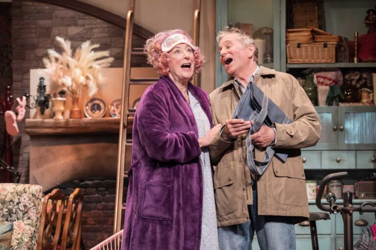 Dame Maureen Lipman as Allegra and John Middleton as Ronen singing together in the cottage kitchen.